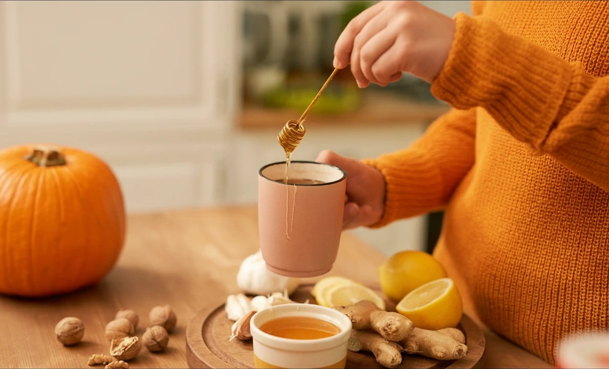 Honey drizzled into a warm mug amid a pumpkin, lemon, ginger and fresh herbs