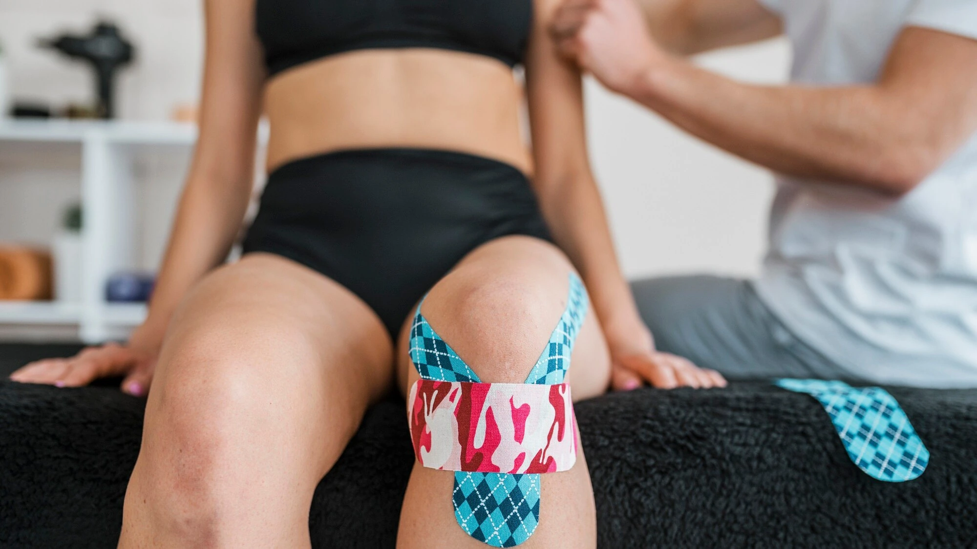 A patient's knee wrapped in therapeutic kinesiology tape during a session